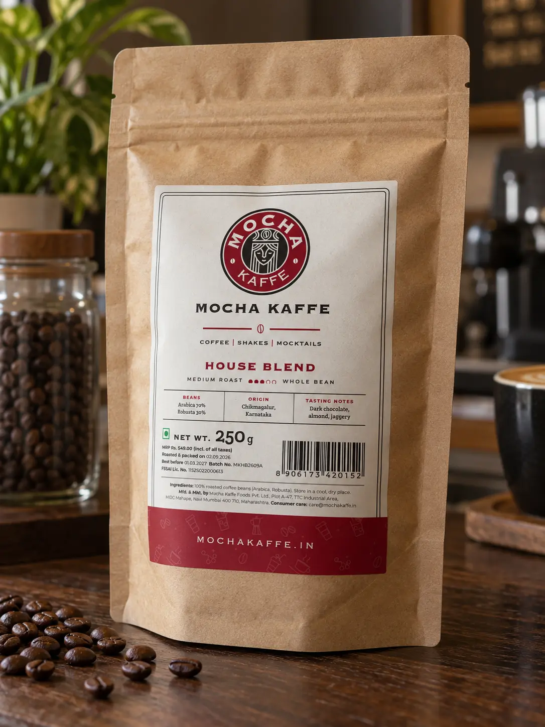 A brown kraft coffee bag with the Mocha Kaffe label on its front, standing on a dark wooden counter beside a few roasted beans.