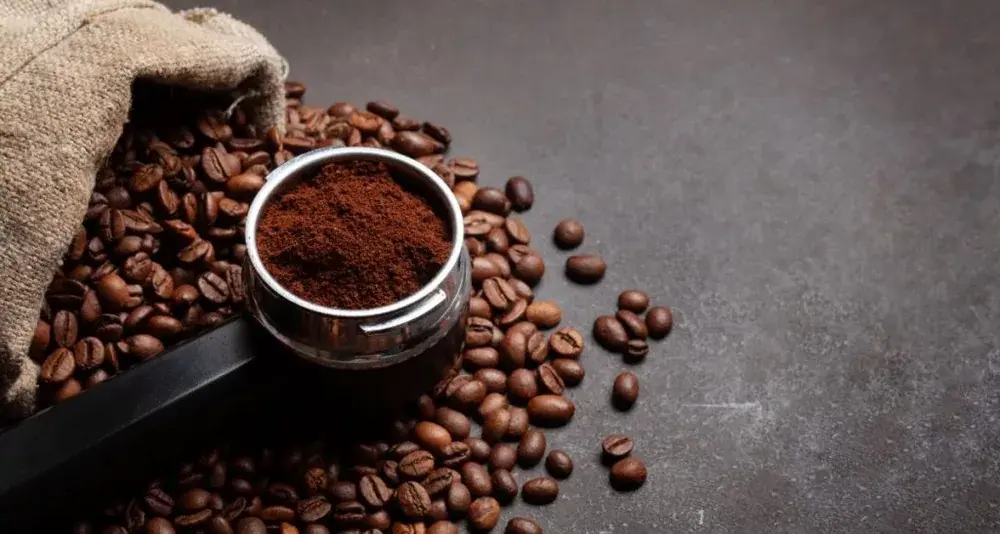 Ground coffee in a portafilter beside a sack of beans.