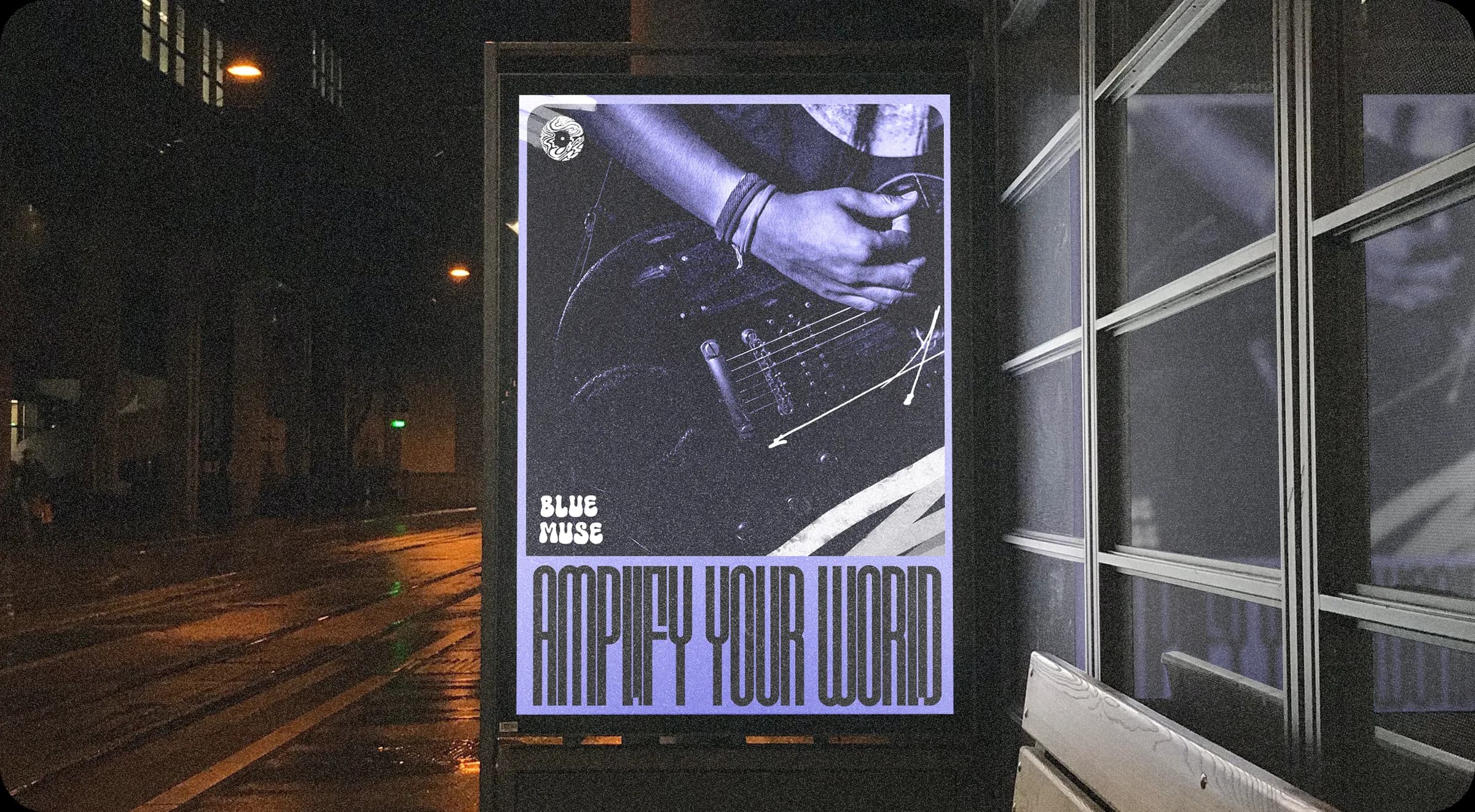A poster in a bus shelter at night: a guitarist’s hands in violet duotone, the logo, and AMPLIFY YOUR WORLD in tall letters.