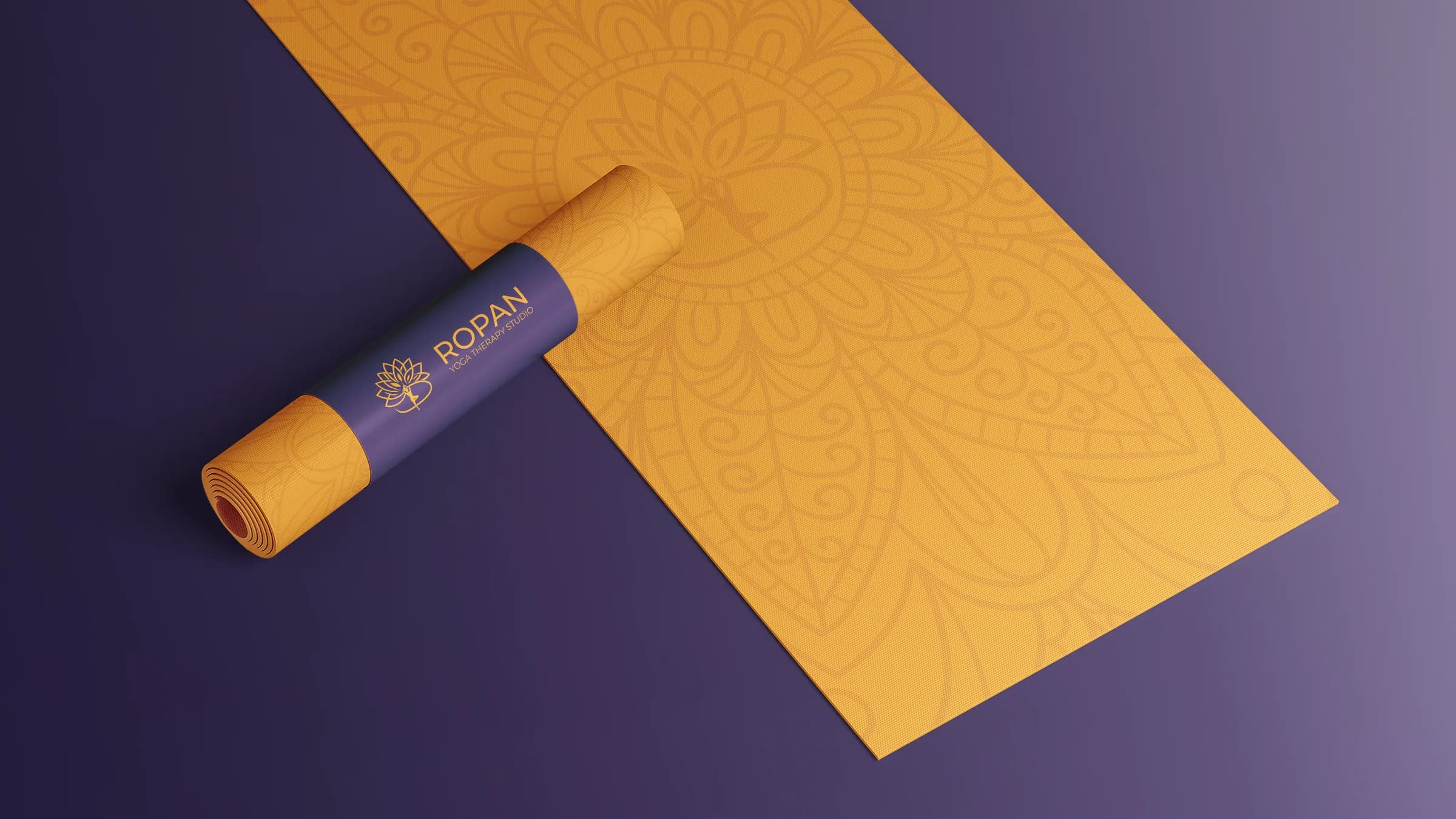 An amber yoga mat printed with the mandala, partly rolled in a purple band with the horizontal logo.