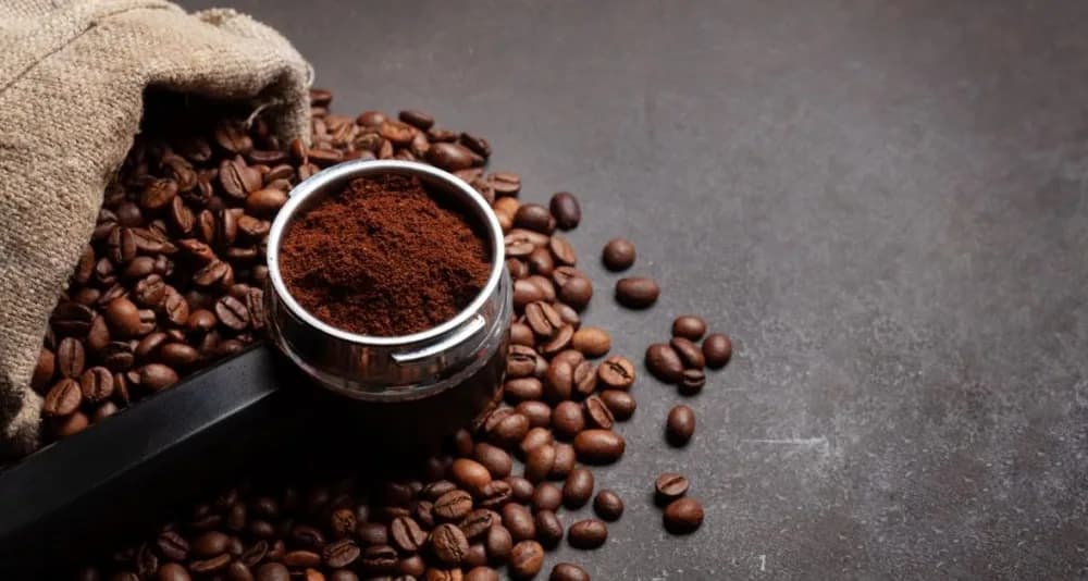 Ground coffee in a portafilter beside a sack of beans.