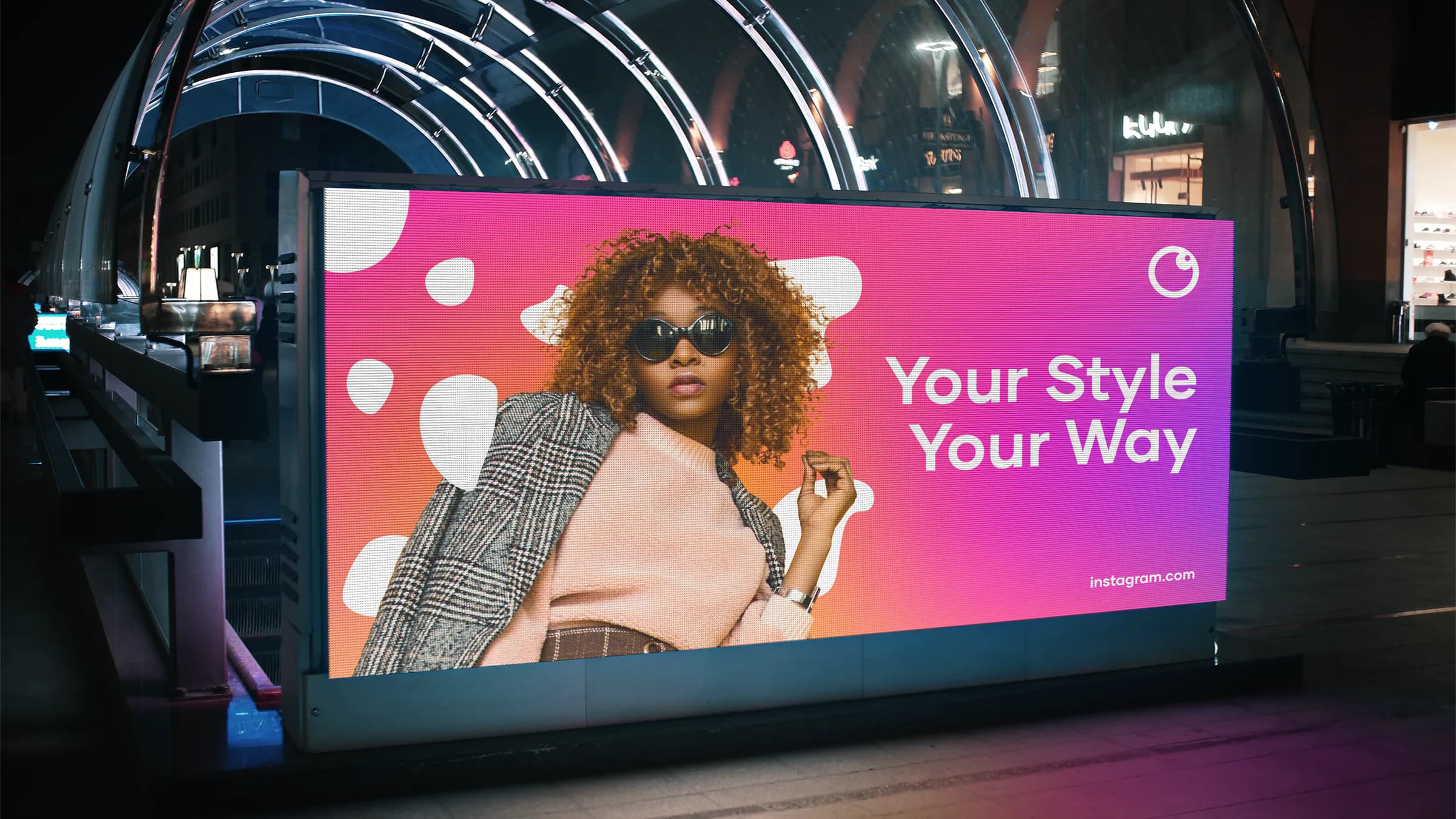 A lit billboard at night: a woman in sunglasses on the pink-to-violet gradient, 'Your Style Your Way', the new mark in the corner