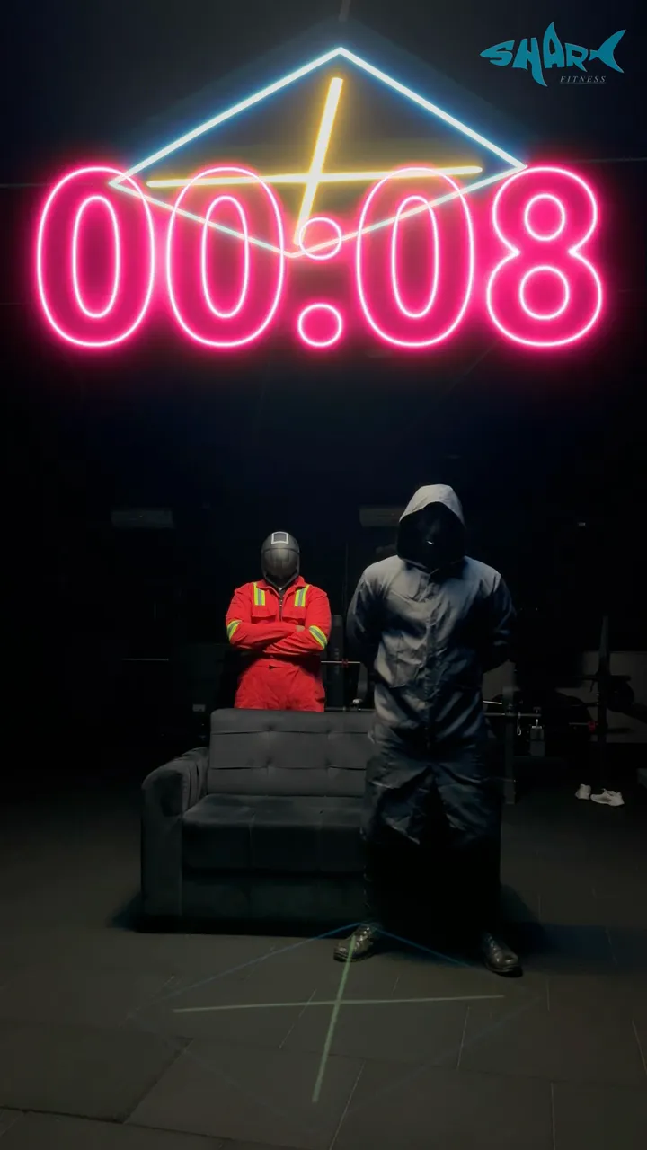A still from the Shark Game teaser: a neon countdown over two masked figures in a dark gym