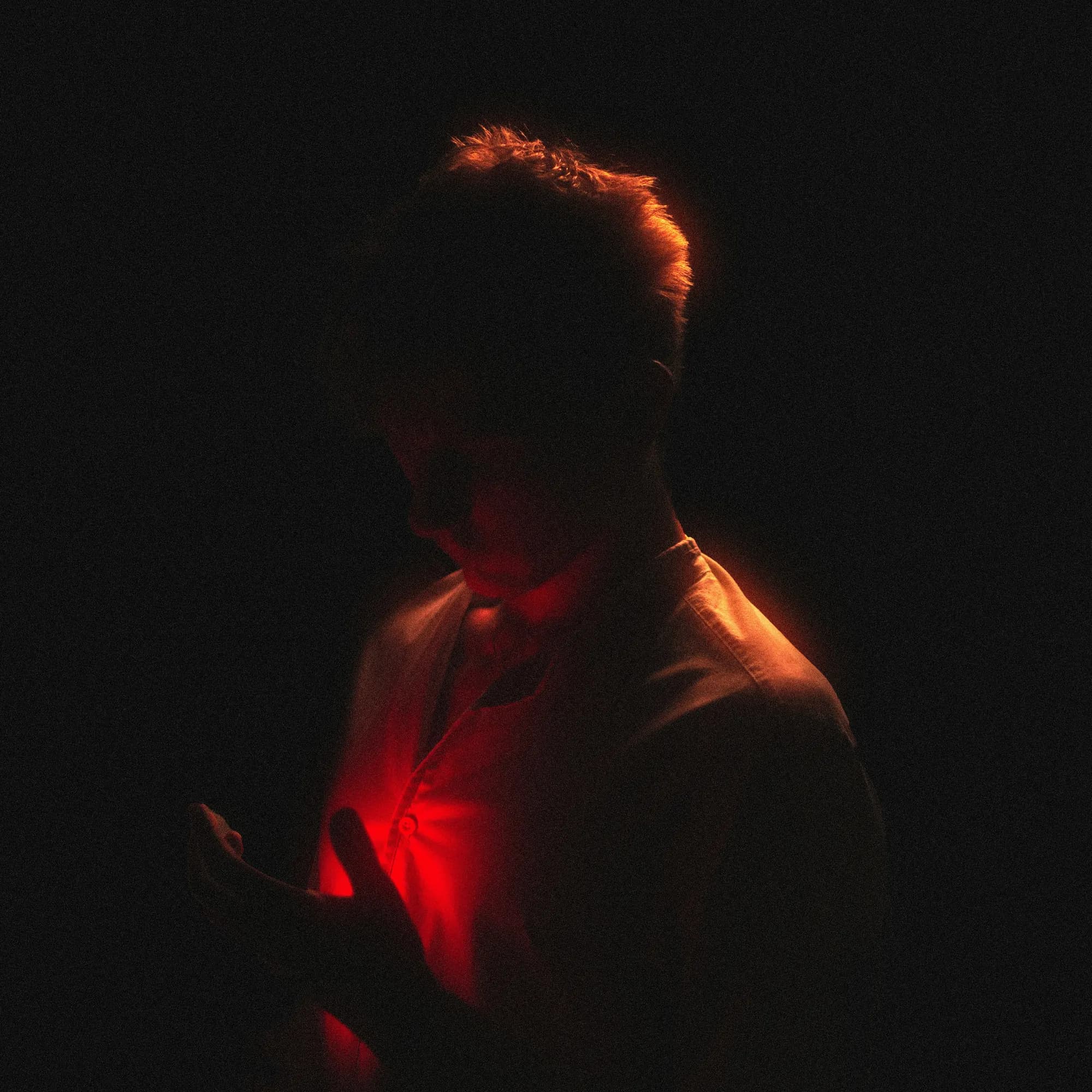 The source photo: a man in the dark, looking down, lit red from below.
