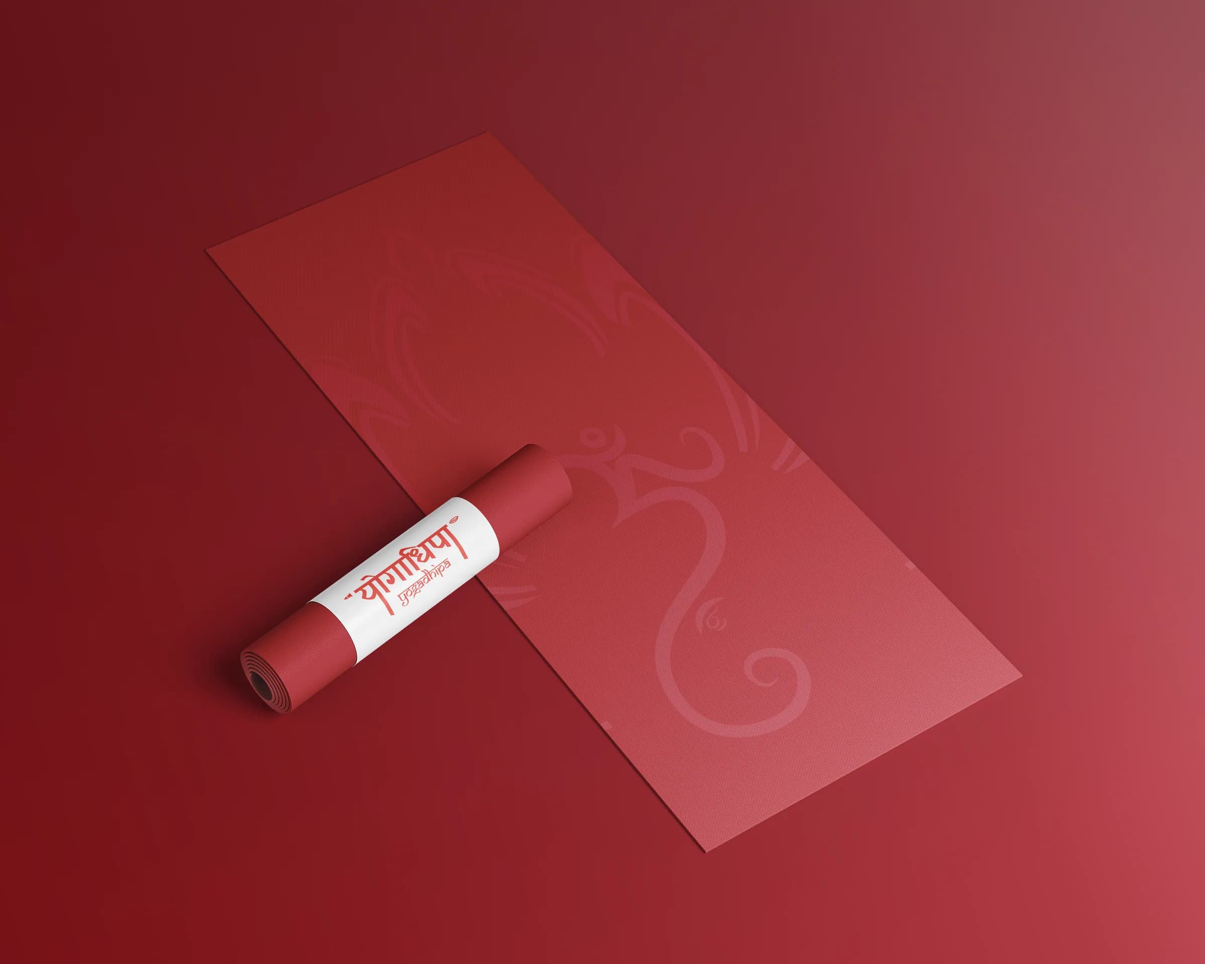 A crimson yoga mat printed tone on tone with the lotus and the Om, one end rolled in a white band with the wordmark.